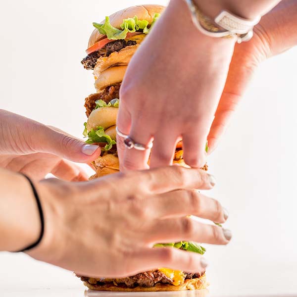 Hands food styling a tower of Shake Shack burgers.