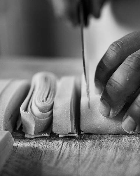 A closup black and white photograph of hands cutting pasta.