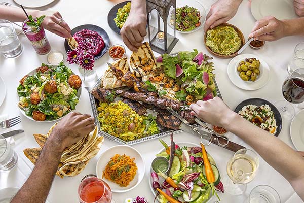 Hands reaching for a spread of delicious greek food at the restaurant Shuka in SoHo.
